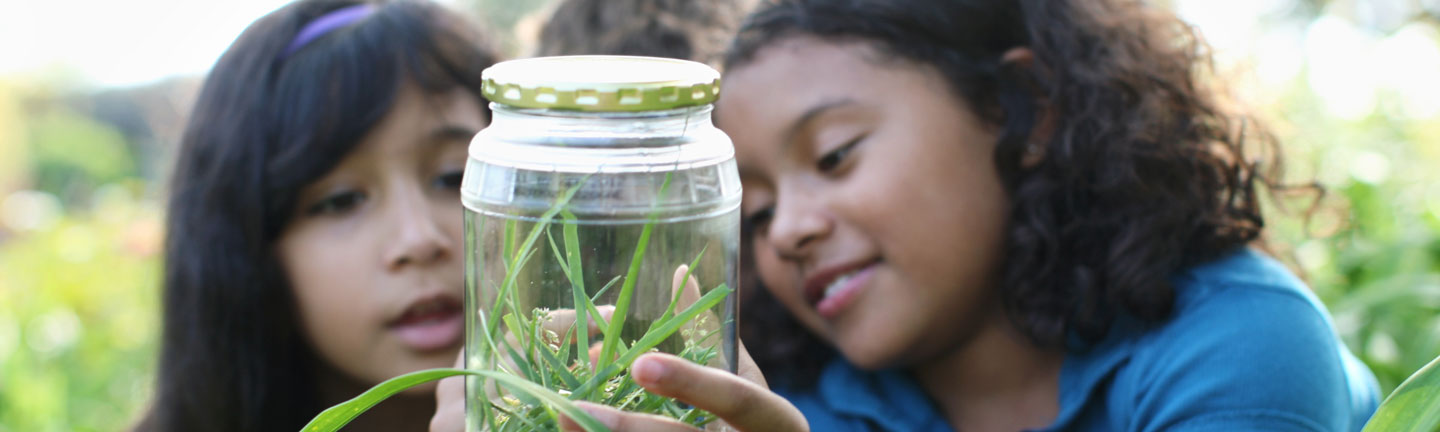 two girls looking into a jar full of grass