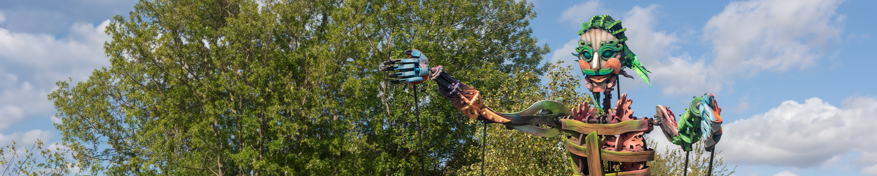 Photograph of 13-foot, multi-coloured sea giant puppet against a blue sky and trees