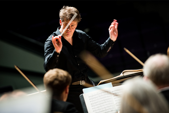 Photograph of the de Havilland Philharmonic Orchestra conductor Robin Browning in front of the orchestra. 