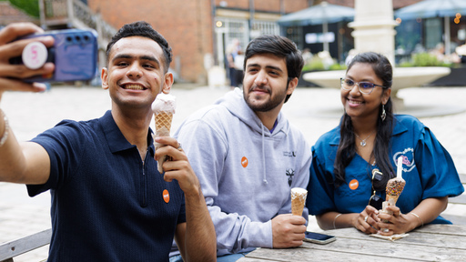 Three students sitting on bench with a phone and ice cream taking a selfie