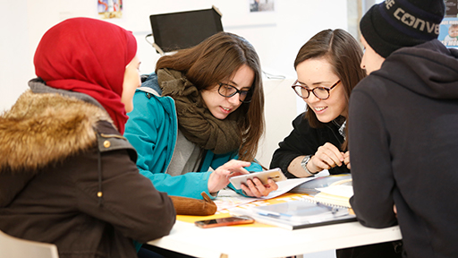 4 students sit around a table looking at a mobile phone