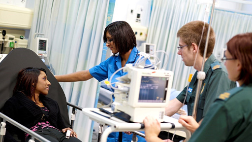 Female nurse talking to a patient in the hospital bed and two paramedics standing in the background